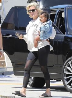 a woman holding a baby while walking down the street with other people behind her and cars