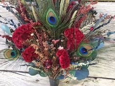 a vase filled with lots of red flowers and peacock feathers on top of a wooden table