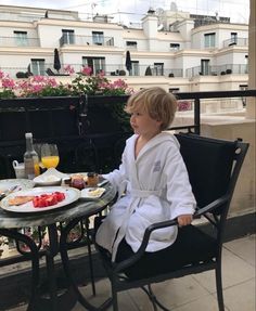 a little boy sitting at a table with food and drinks on it, outside in the sun