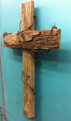 a cross made out of wood with barbed wire on the top and bottom part, against a blue wall