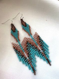 two pairs of beaded earrings with brown and blue beads on white fabric, sitting on top of each other