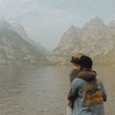 a person standing in front of a body of water with mountains in the back ground