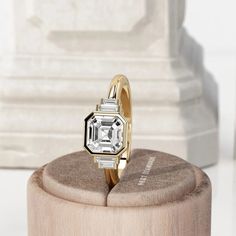 an engagement ring sitting on top of a wooden stand in front of a white statue