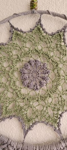 a crocheted doily is displayed on the wall with a small green object