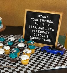 a table topped with lots of cupcakes next to a sign that says start your engines put it in gear and let's celebrate second