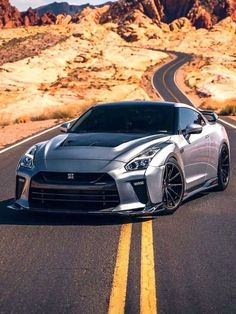 a silver sports car parked on the side of a road in front of some mountains