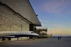 an airplane parked in front of a large building with people standing around it at sunset