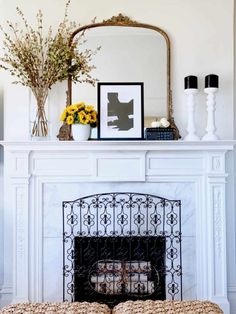 a fireplace with a mirror, vases and flowers on the mantel above it