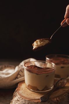 someone is spooning some kind of dessert out of a small glass bowl on a piece of wood