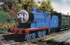 a thomas the tank engine is riding on train tracks with trees and bushes in the background