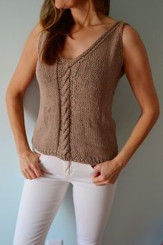 a woman standing in front of a wall wearing white pants and a brown knitted top