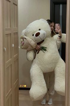 a woman holding a large white teddy bear in her arms while taking a selfie