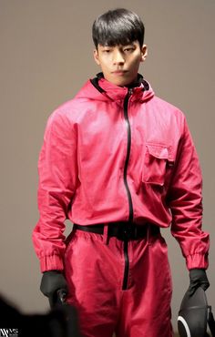 a male model in a red outfit and black gloves on the catwalk, looking at the camera