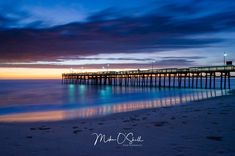 a pier at the end of a beach with blue water and clouds in the background