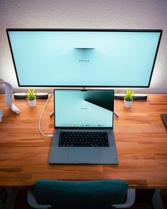 an open laptop computer sitting on top of a wooden desk next to a large monitor