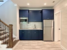 a kitchen with blue cabinets and stainless steel refrigerator freezer next to wooden staircase leading up to the second floor