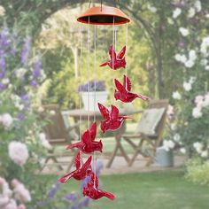 a red bird wind chime hanging from a tree in front of some pink flowers