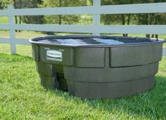 a large plastic tub sitting in the grass near a white fence and some green grass