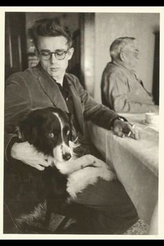 a man sitting at a table with a dog in his lap and another man standing behind him