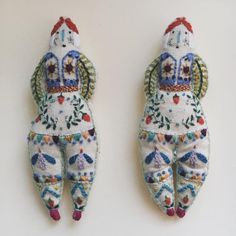 two handmade dolls are hanging on the wall together, one is wearing an elaborately decorated outfit