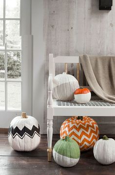 white pumpkins sitting on top of a wooden bench next to a blanket and window