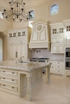 a large kitchen with marble counter tops and white cabinets, chandelier above the island