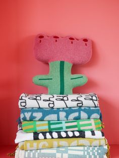 a stack of folded towels with a stuffed cactus on top, against a pink background