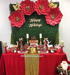 a table topped with red and gold christmas decorations next to a wall covered in fake flowers