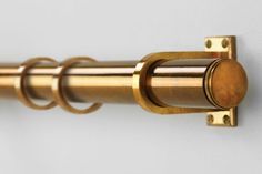 a close up of a metal curtain rod on a white wall with gold colored hardware