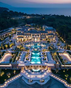 an aerial view of a mansion at night with lights on the pool and surrounding landscaping