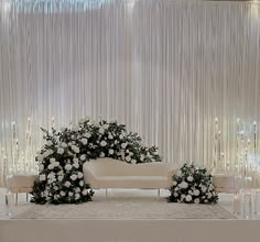 a wedding setup with white flowers and candles on the floor, in front of a curtained wall