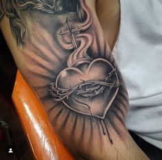 a man with a cross and heart tattoo on his arm