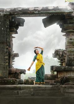 a woman in a yellow and green sari standing on the edge of a stone structure