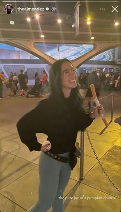 a woman standing in front of a metal fence holding a baseball bat and smiling at the camera