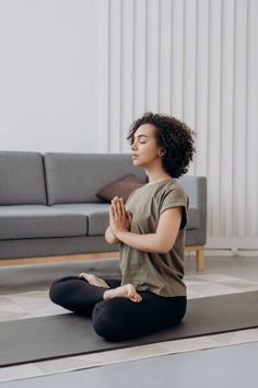 a woman is sitting on the floor and meditating with her hands clasped in front of her face