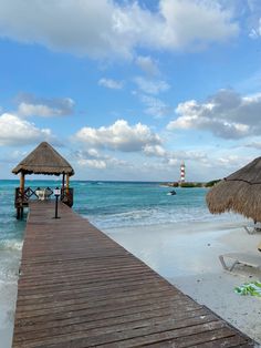 a wooden dock leading to the beach with thatched umbrellas