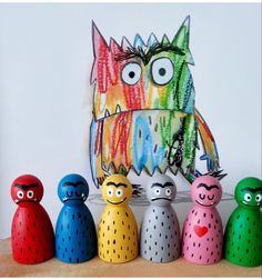 five colorfully painted wooden toys are lined up in front of a drawing of an owl