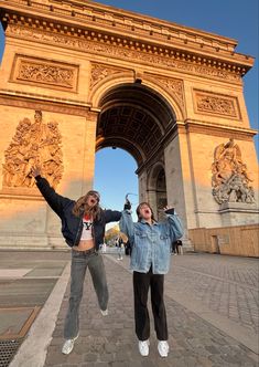 two girls jumping in front of the arc de trioe