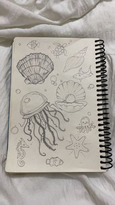 an open notebook with drawings of sea animals and jellyfishs on it, sitting on a white sheet