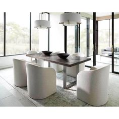 a dining room table with white chairs and a bowl on top of it in front of large windows