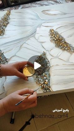 a woman is working on an art project with gold and silver paint in her hands