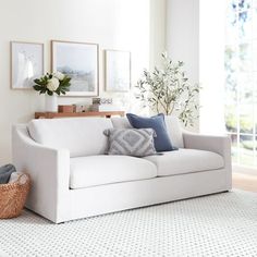 a living room with a white couch and some pictures on the wall above it in front of a window