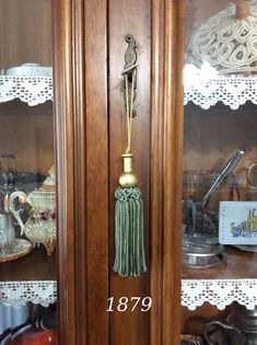 a wooden door with a brass handle and tassel on the side, in front of lace doily