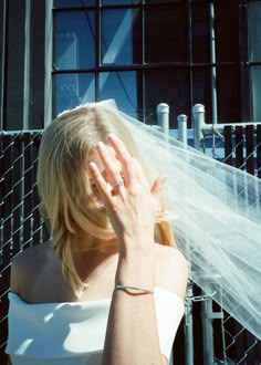 a woman in white dress holding her hand up to her face with veil over her head