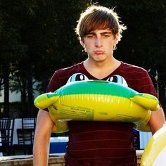 a young man is holding an inflatable frog float on his chest and looking at the camera