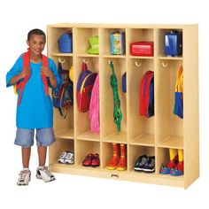 a young boy standing next to a wooden locker with shoes and backpacks on it