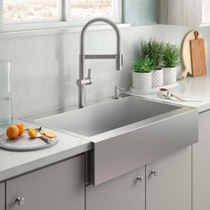 a stainless steel kitchen sink with two oranges and a cutting board on the counter