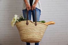 a woman holding a large woven basket with vegetables in it