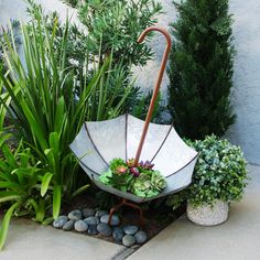 an umbrella shaped planter sitting in the middle of a garden with rocks and plants around it