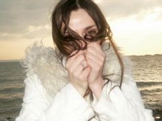 a woman covers her face with her hands near the ocean